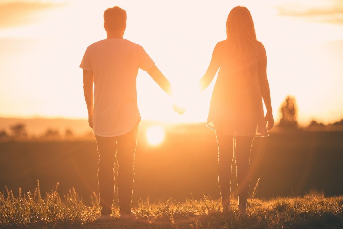 A silhouette of a couple holding hands facing the sunrise.