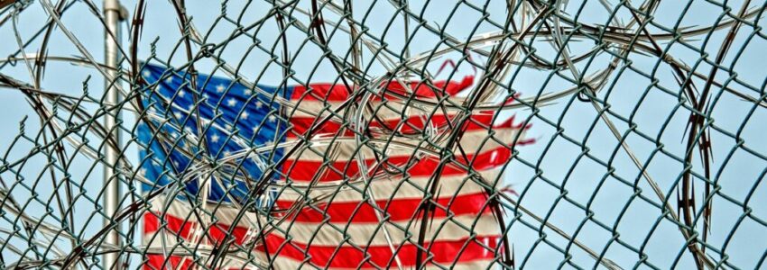 A private prison's fence with an American flag on the background.
