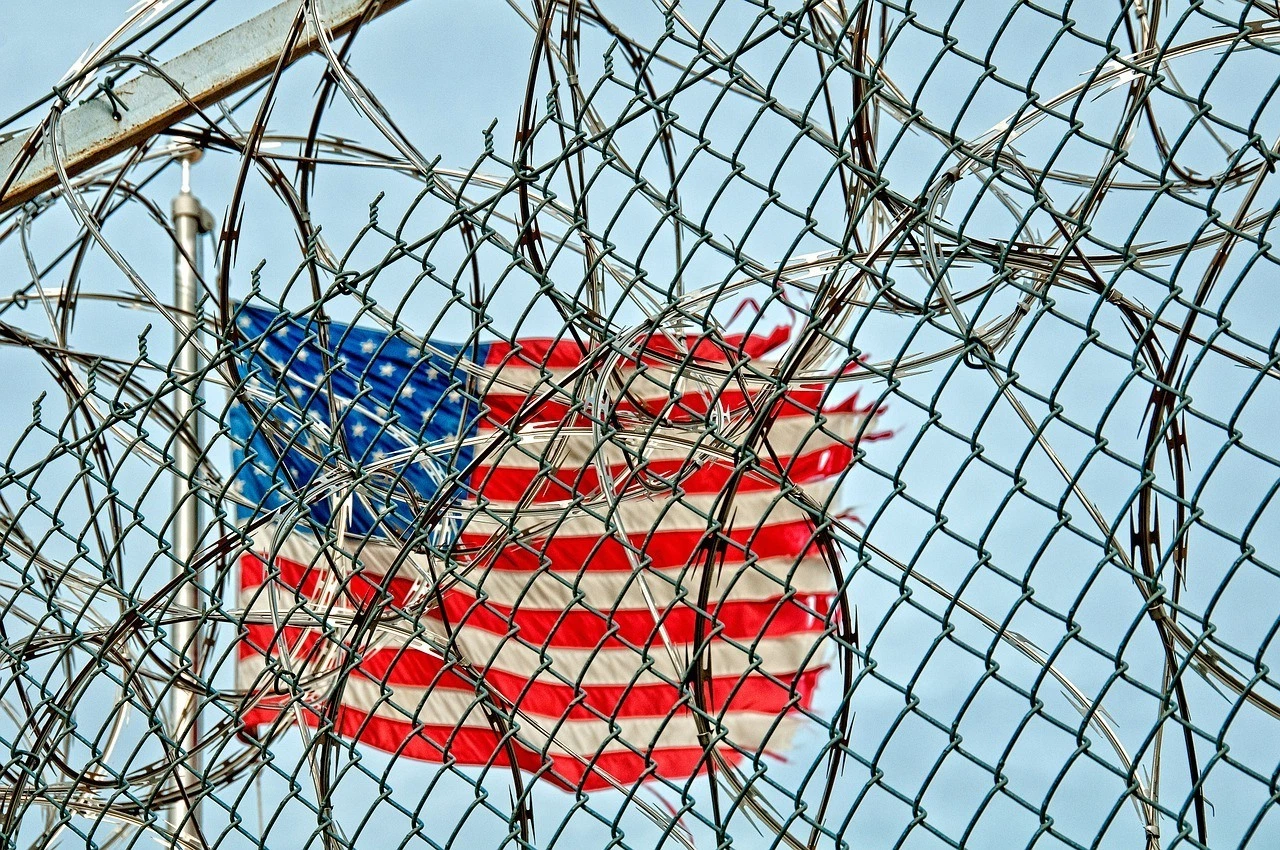 A private prison's fence with an American flag on the background.