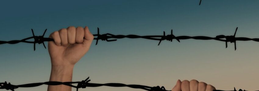 An inmate holding on to a barbed prison fence.