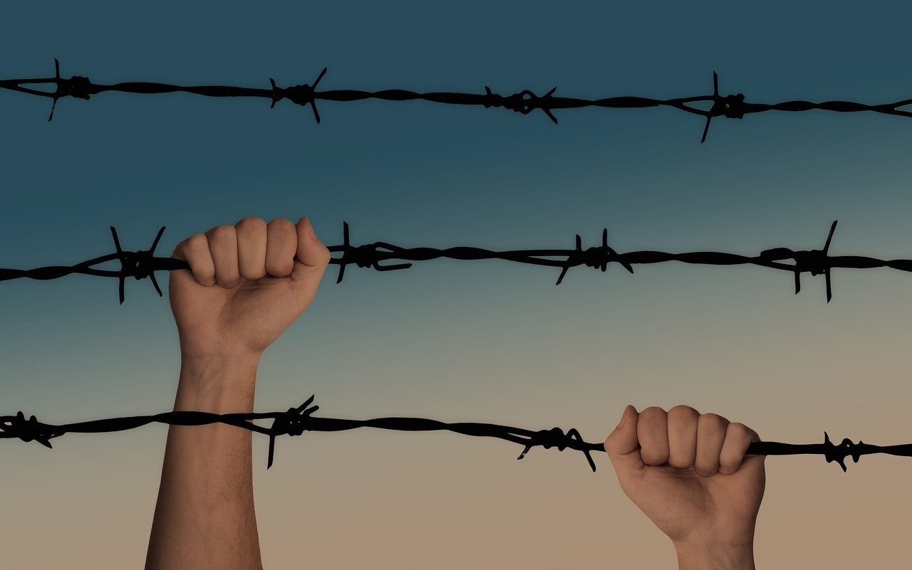 An inmate holding on to a barbed prison fence.