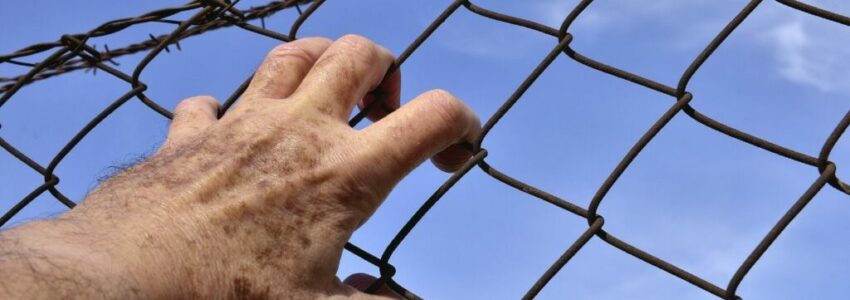 A man holding on to a prison fence preparing for his reentry.