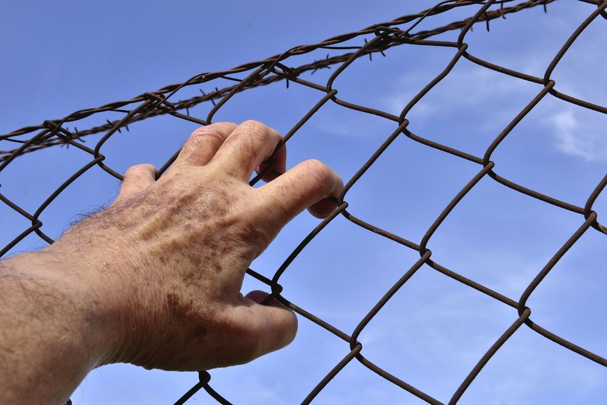 A man holding on to a prison fence preparing for his reentry.