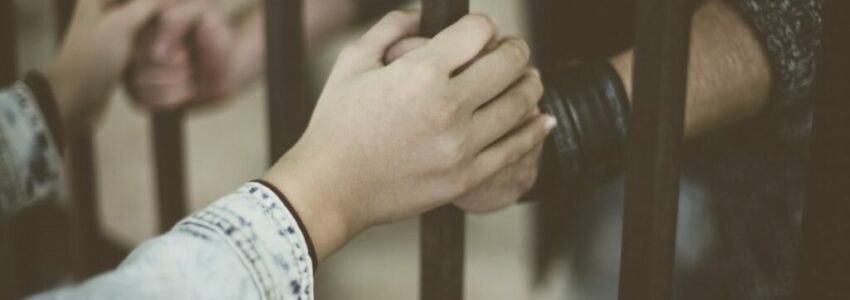 An inmate holding hands with his penpal through the jail bars.