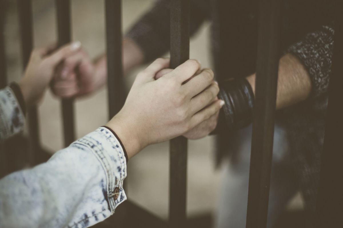 An inmate holding hands with his penpal through the jail bars.