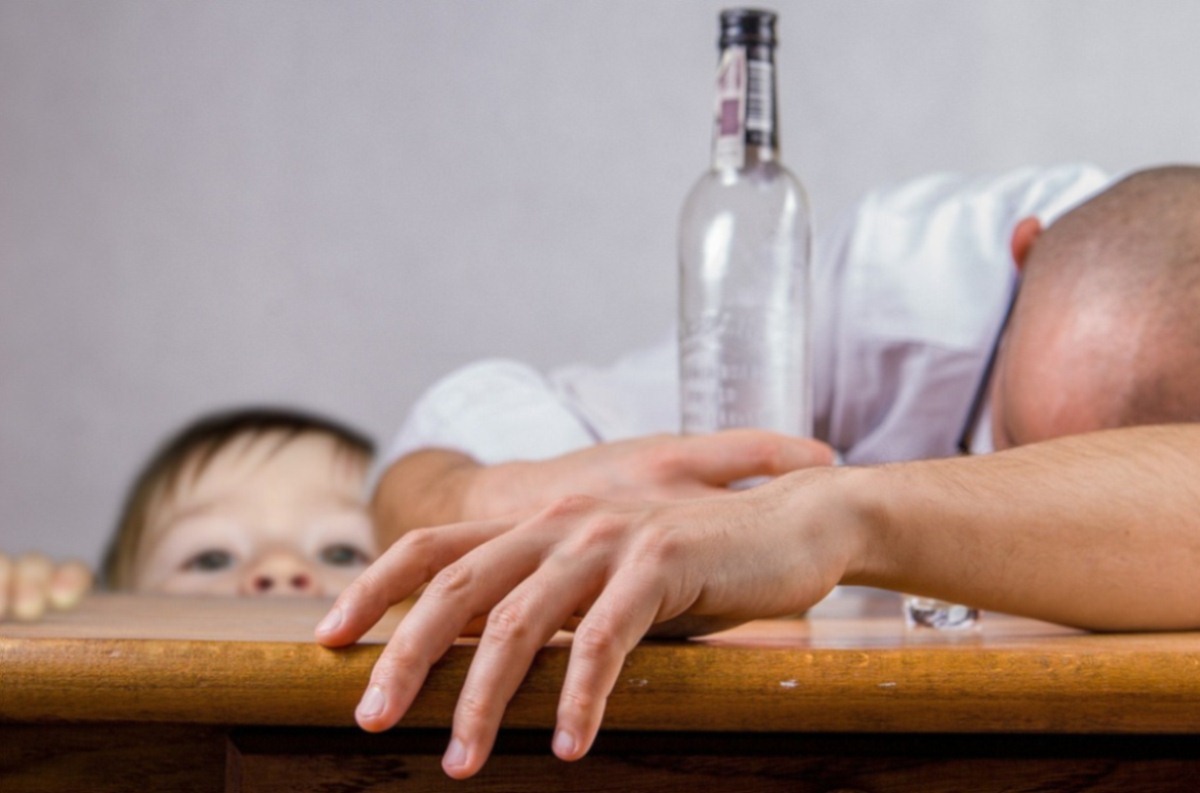 A daughter looking over the table at her sleeping intoxicated father.