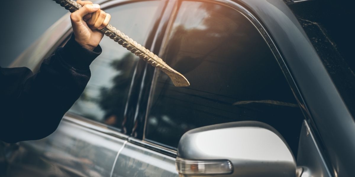 A poor robber dressed in black holding crowbar at a driver in a car.