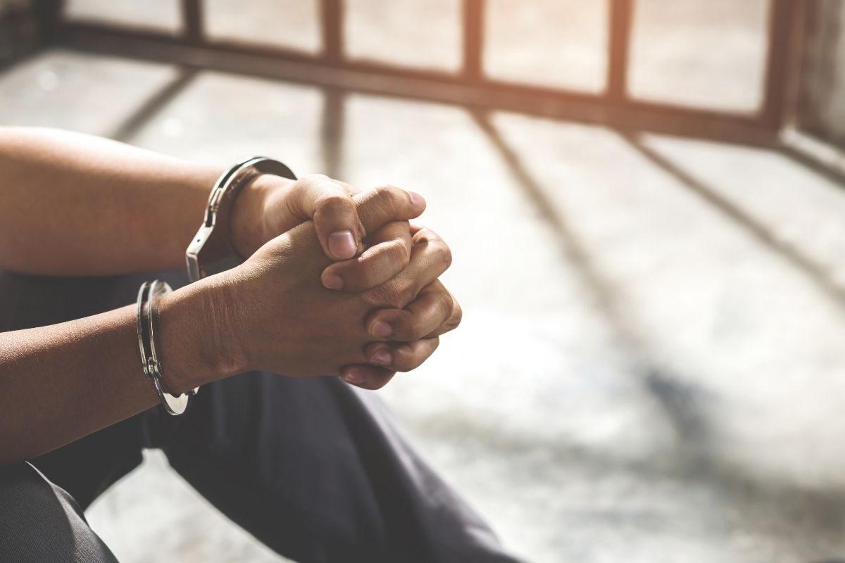 A man in handcuffs sitting inside a prison cell.