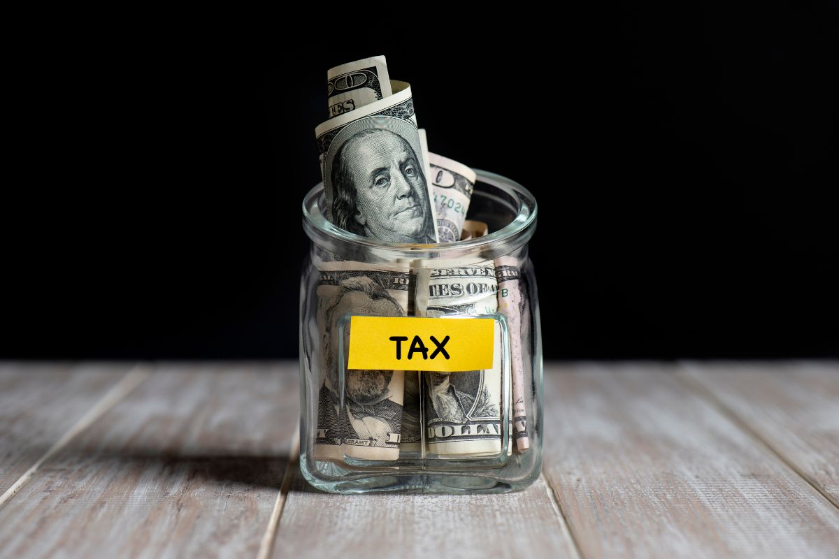 Dollar bills inside a glass jar labeled "tax".