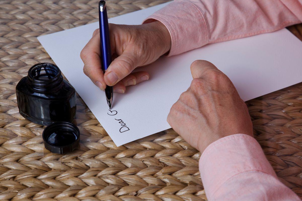 man's hand writing a letter of encouragement in a white paper