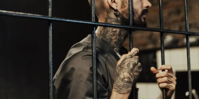 A prisoner holding the bars showing his tattoos and a lightning bolt tattoo