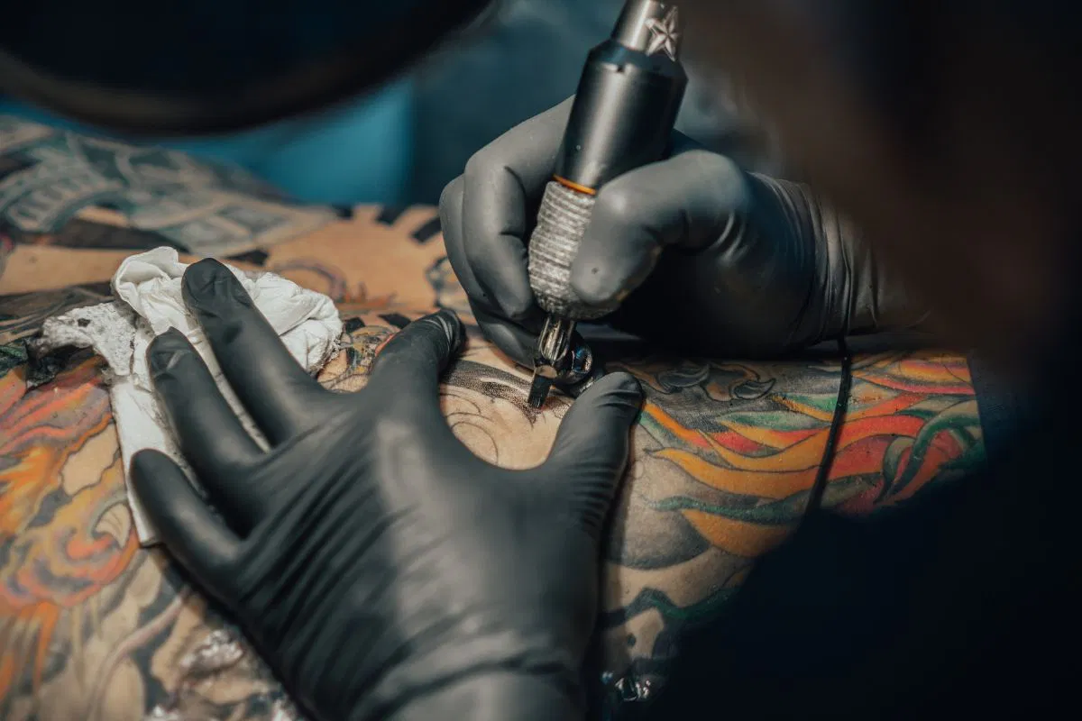 An artist tattooing a person's skin with a lightning bolt tattoo